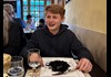 A teenager eating cuttlefish ink spaghetti in a Venetian restaurant.