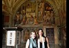 Two tourists having their picture taken in front of the School of Athens. 