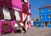 Two women sitting on a bench in Burano in front of colorful houses.
