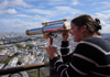 A woman using a telescope while visiting the Eiffel Tower.